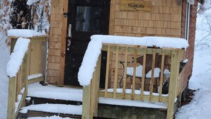 Une cabane en bois avec un porche et des marches couverts de neige.