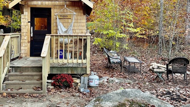 Une petite cabane en bois avec une véranda, une porte noire et un hamac.