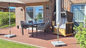 Une terrasse extérieure avec une table et des chaises, un espace salon abrité et un mur en briques.