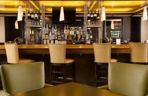 Een bar met meerdere krukken en een bar, volgepakt met flessen.