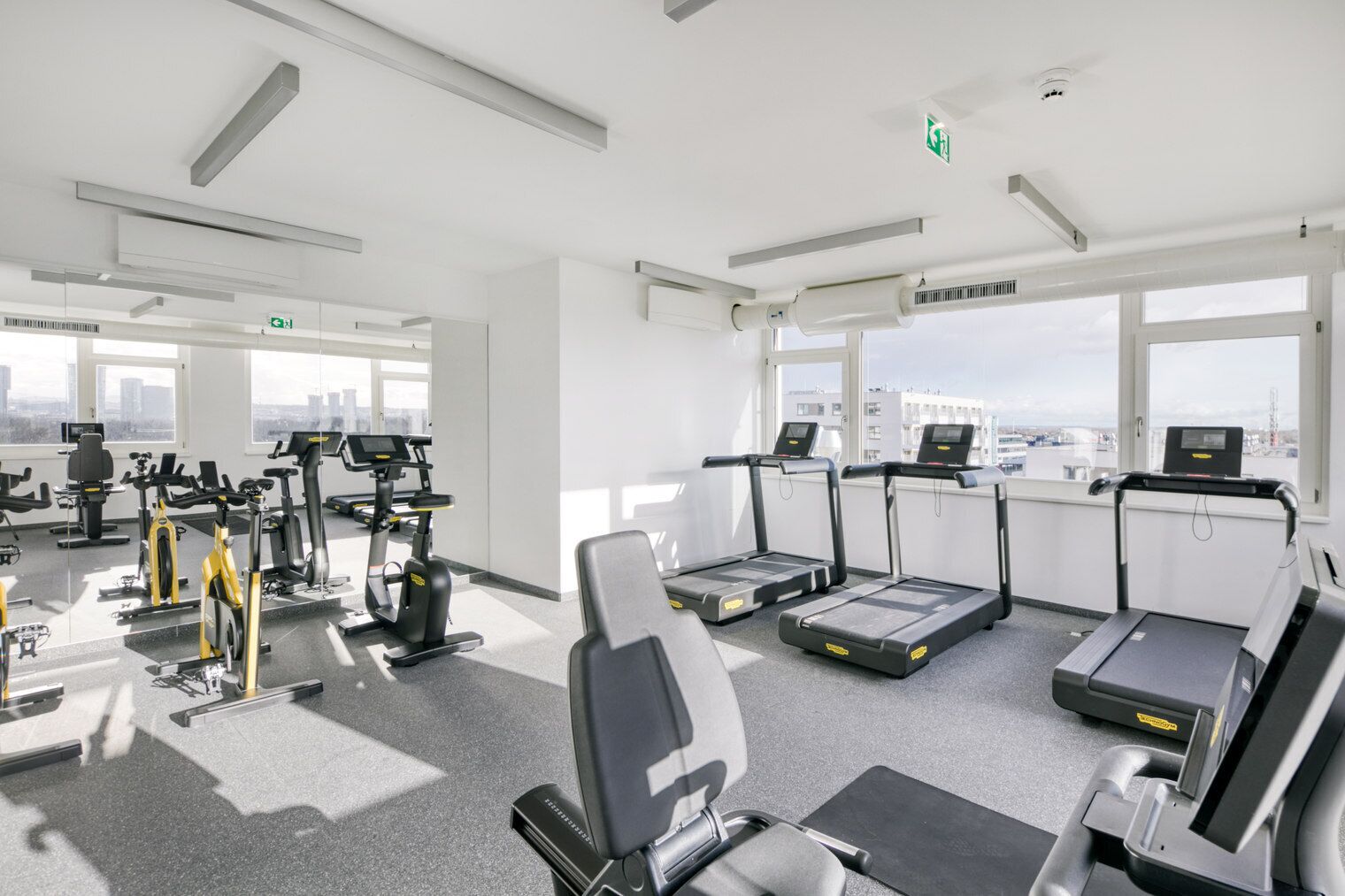 Ein modernes Fitnessstudio mit verschiedenen Trainingsgeräten, großen Fenstern und Blick auf die Stadt.