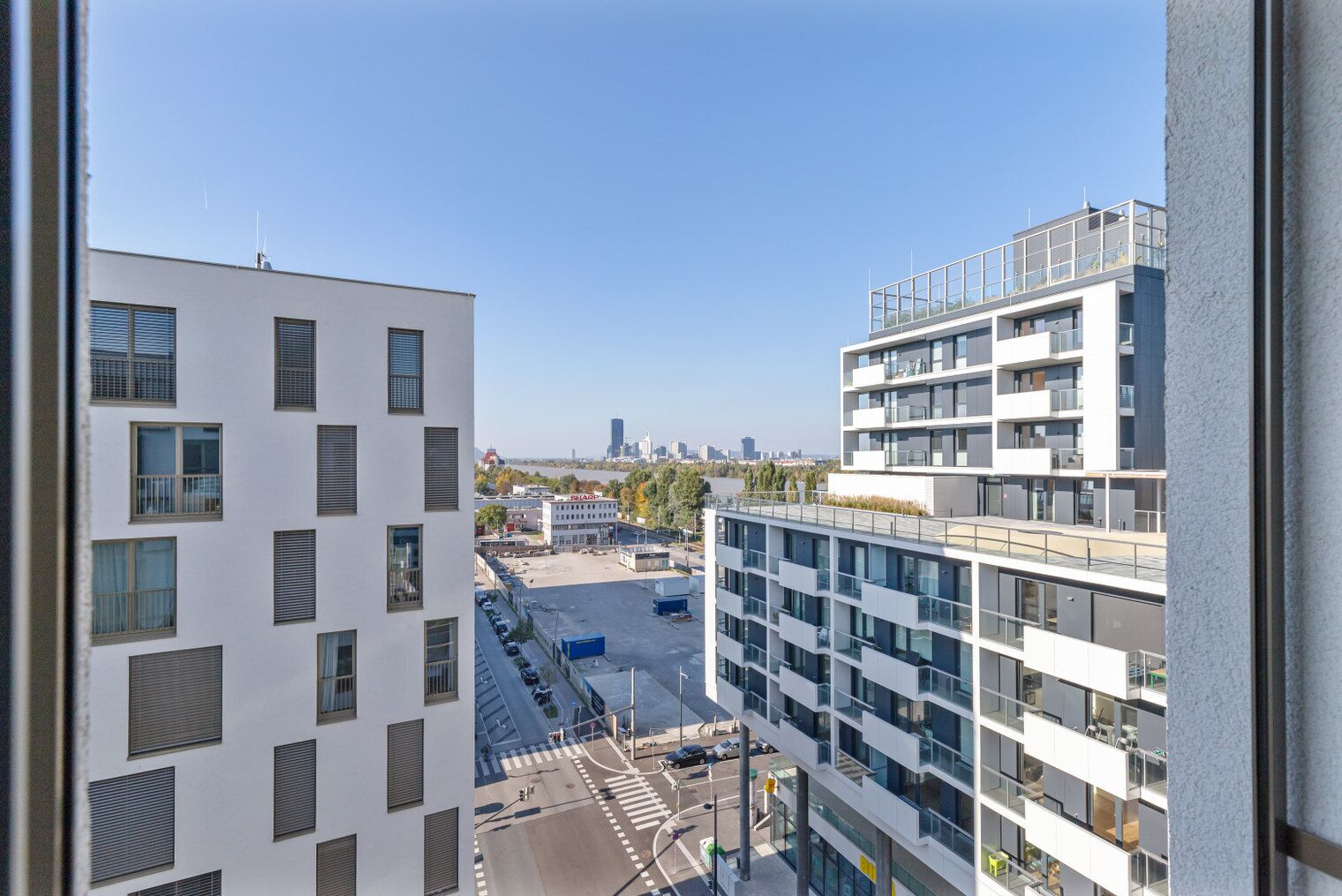 Ein modernes Gebäude mit mehreren Stockwerken, großen Fenstern und Blick auf eine Stadtlandschaft im Hintergrund.