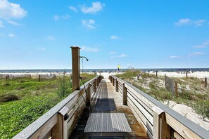 Une promenade en bois menant à une plage, avec une grille métallique à son extrémité.