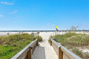 A wooden boardwalk leading to a sandy beach with a flag in the distance.