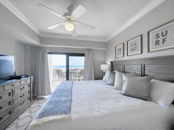 A hotel room with a bed, a television, a ceiling fan, and a view of the ocean.