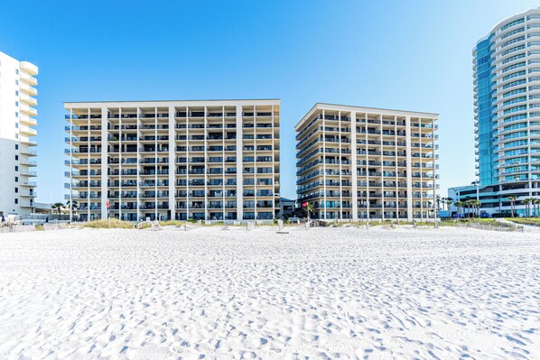 A beachfront hotel with multiple floors, balconies, and a sandy beach in the foreground.