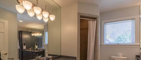 A modern bathroom with a granite countertop sink, dark cabinets, a large mirror, a shower with a curtain, and a toilet with a bidet attachment.