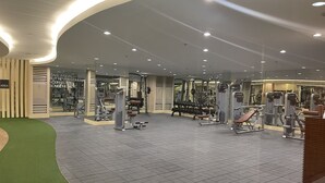 Une salle de sport moderne équipée de divers appareils d’exercice, d’un espace recouvert d’une moquette verte et d’un grand mur miroir.