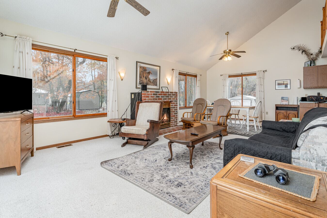 A cozy living room with a fireplace, comfortable seating, and large windows offering a view of trees.