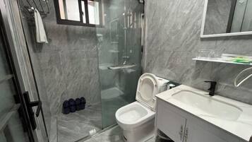 Un baño moderno con ducha acristalada, inodoro blanco y lavamanos blanco con espejo superior.