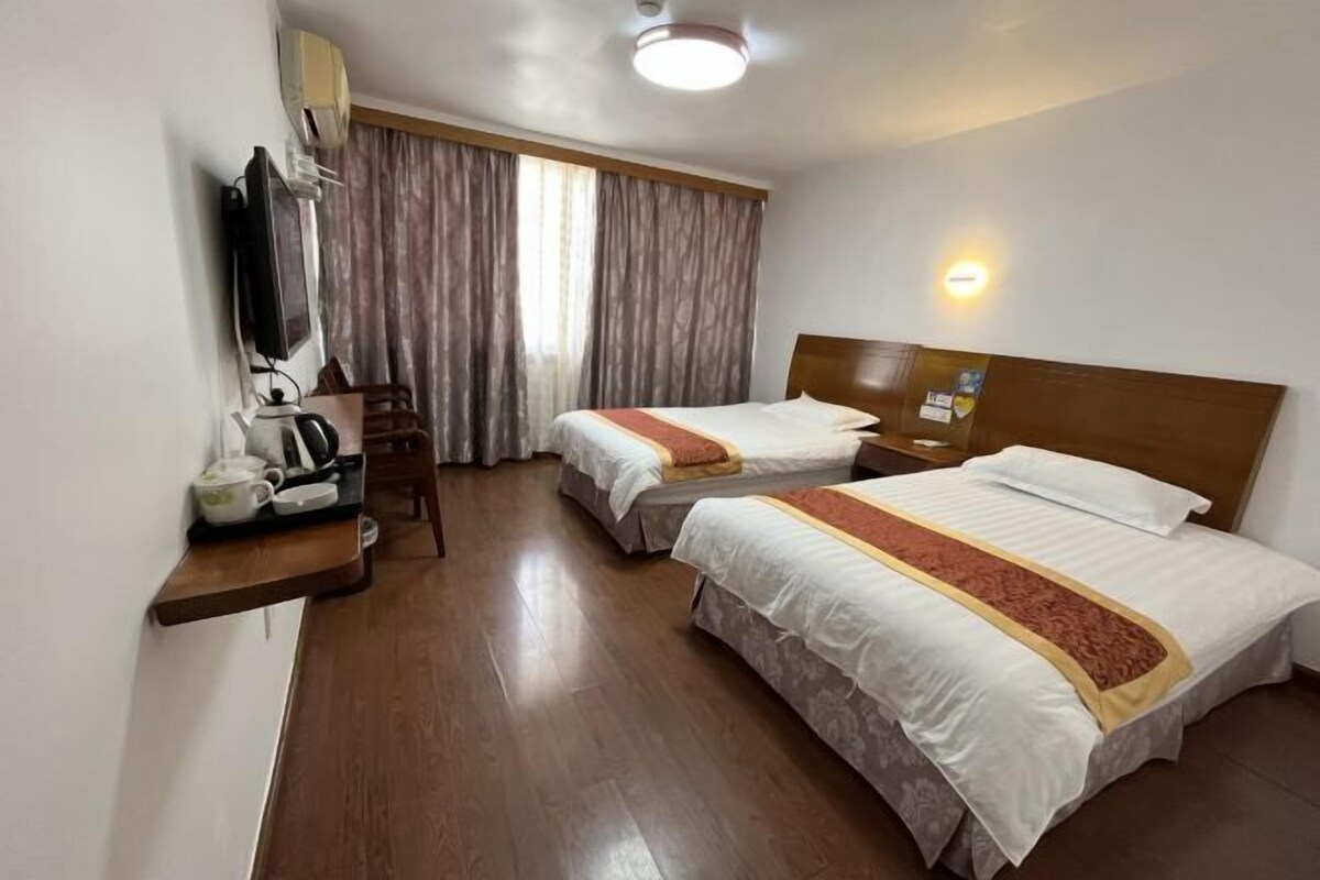 A hotel room with two beds, a TV, a desk with a kettle, and a window with curtains.