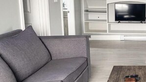 A modern living room with a grey sofa, a wooden coffee table, and a flat-screen TV mounted on a white entertainment unit. - Unique Modern Luxury 2 Bedroom Apartment (Chapleau)