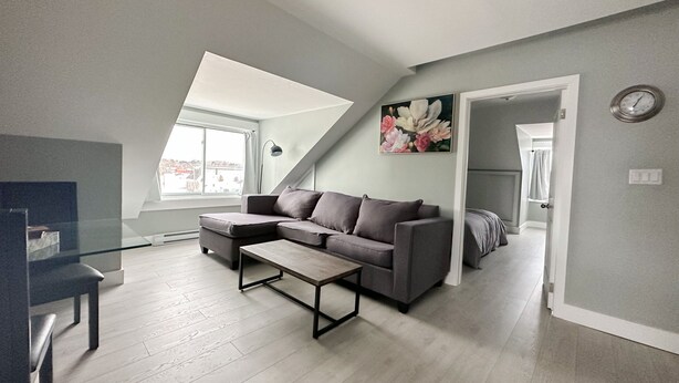A modern living room with a sectional sofa, a coffee table, and a view of the city through a large window. - Unique Modern Luxury 2 Bedroom Apartment (Chapleau)