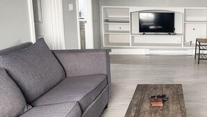 A modern living room with a grey sofa, a wooden coffee table, and a flat-screen TV mounted on a white wall. - Unique Modern Luxury 2 Bedroom Apartment (Chapleau)