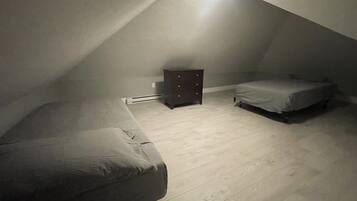 Une petite pièce mansardée, faiblement éclairée, avec un plafond en pente, une seule commode en bois et deux lits.