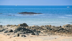 A rocky beach with clear blue water and a sailboat in the distance.