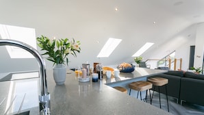 A modern kitchen with a central island, a built-in sink, and a dining area with a sofa and stools.
