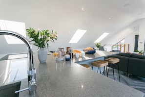 Una cocina moderna con una isla central, un lavamanos empotrado y una zona de comedor con un sofá y taburetes.