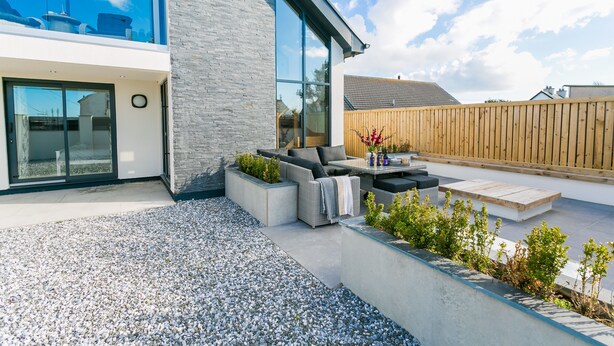 A modern outdoor patio with a seating area, a wooden fence, and a gravel ground.