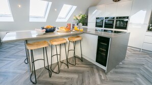 A modern kitchen with a central island, bar stools, a clock, and skylights.