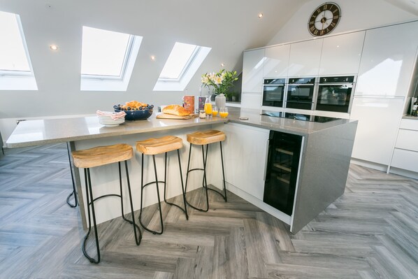 Et moderne køkken med en central ø, barstole, et ur og ovenlys.