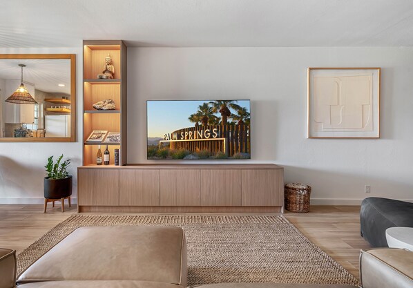 Una sala de estar moderna con un televisor de pantalla plana grande montado sobre un mueble de madera, un espejo grande y una obra de arte enmarcada en la pared.