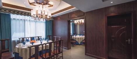 A dining area with a round table, chairs, and a chandelier. There is a wooden door and a mirror on the wall.