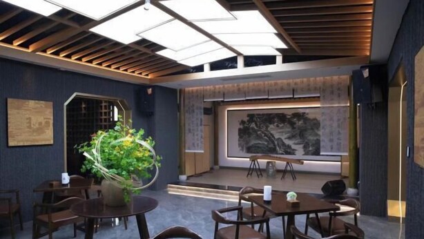 A modern dining area with wooden tables and chairs, a large painting on the wall, and a ceiling with skylights. - Long Cheng Hotel (Xiangxiang)