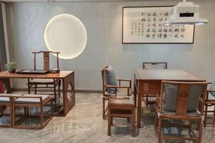 A room with a round table, chairs, a small table with a lamp, and a wall with a framed text.