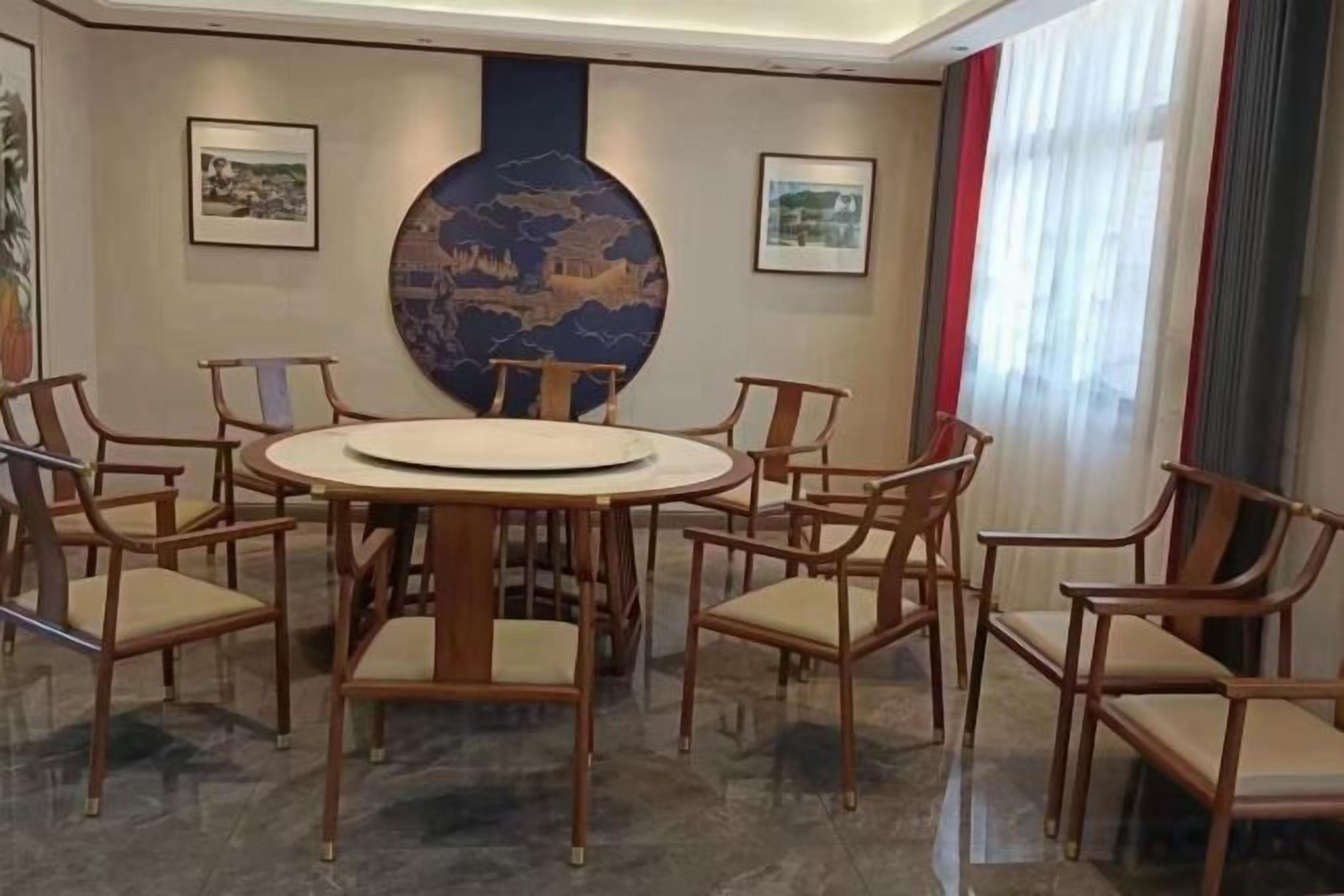 A conference room with a round table surrounded by chairs, a large vase, and framed pictures on the walls.