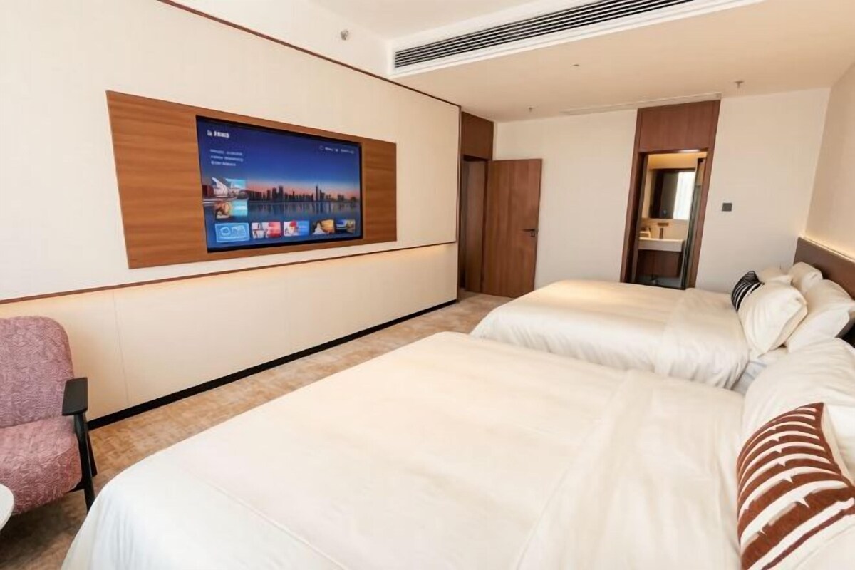 Ett hotellrum med två sängar, en tv som är monterad på väggen, en stol och ett badrum med en spegel.