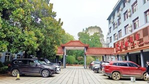 A parking area with cars, a traditional archway, and a building with signage. - Long Cheng Hotel (Xiangxiang)