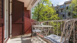 Een balkon met een metalen stoel en tafel, een potplant en uitzicht op een gebouw en bomen.