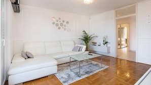 Een moderne woonkamer met een witte leren bank, een glazen salontafel en een decoratief wandobject.