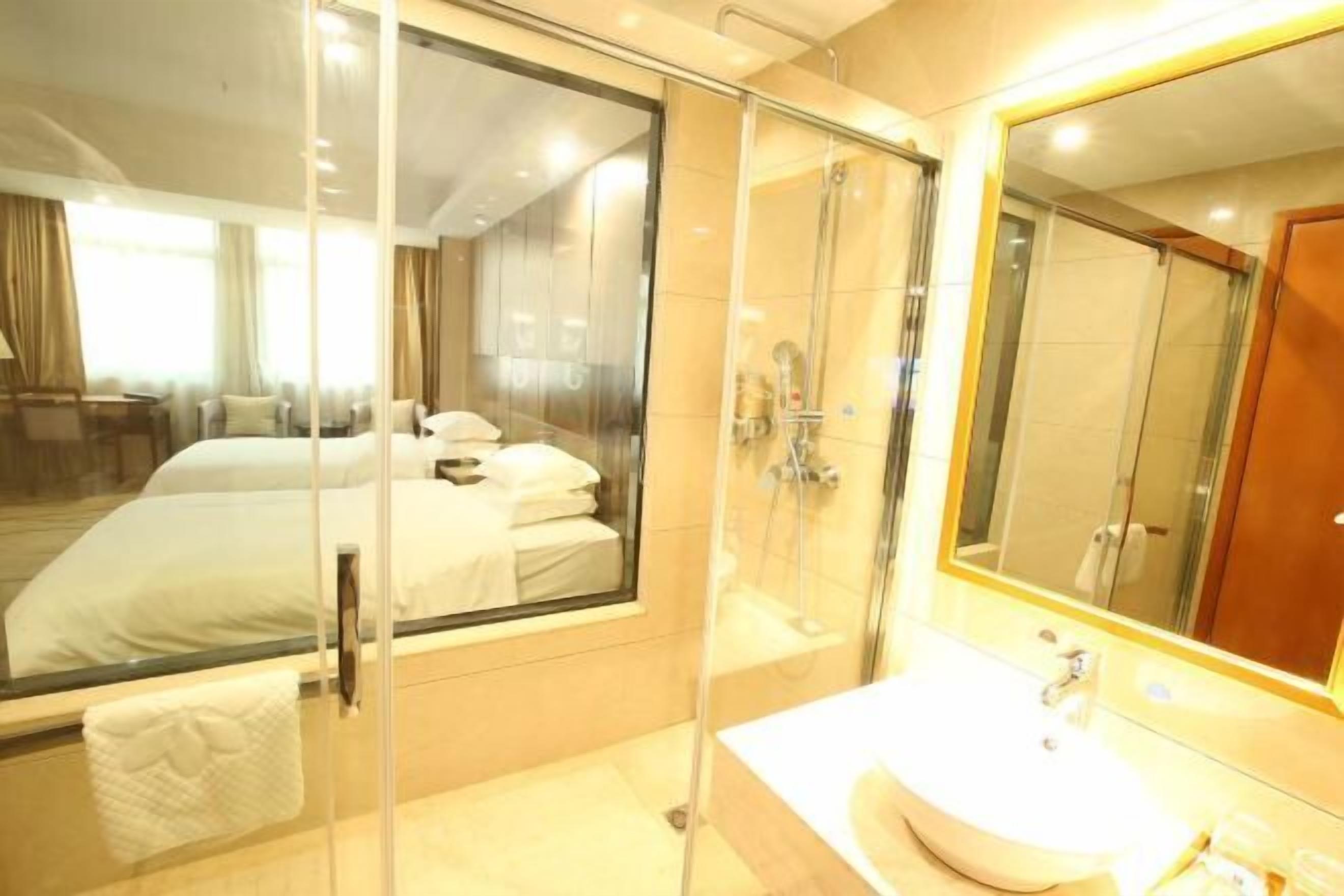 A hotel room with a bed, a glass-enclosed shower, a sink, and a large mirror.