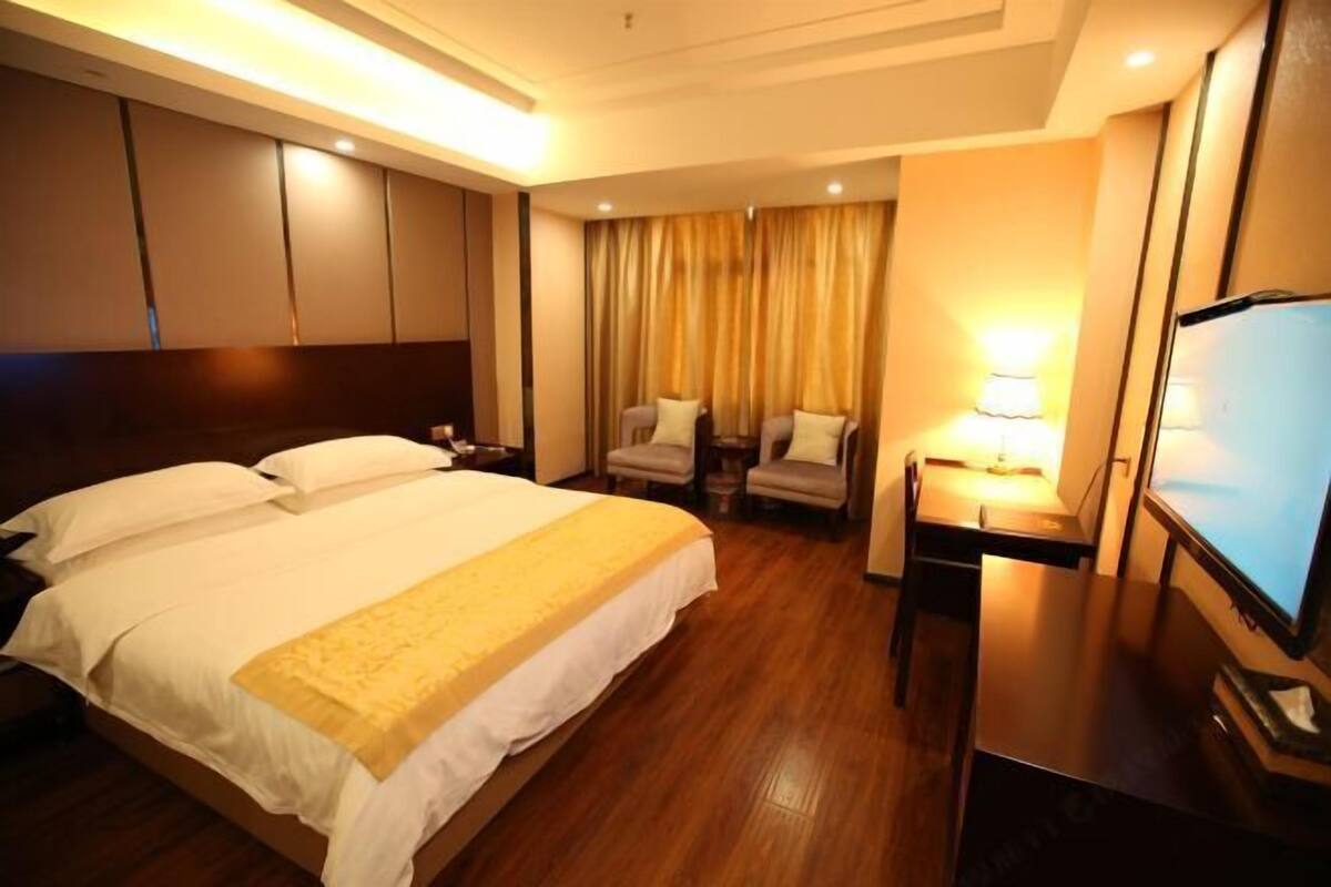 A hotel room with a bed, a desk, a chair, a TV, and a lamp.