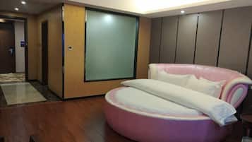 A modern hotel room with a wooden floor, a pink and white circular bed, a large sliding door, and a view of the hallway.