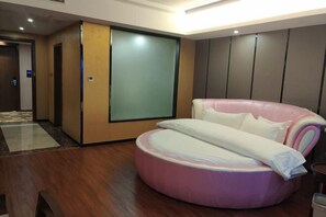 A modern hotel room with a wooden floor, a pink and white circular bed, a large sliding door, and a view of the hallway. - Donghu Hotel (Shouning)