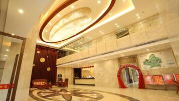 A hotel lobby with a reception desk, a large circular decorative floor pattern, and a modern chandelier.