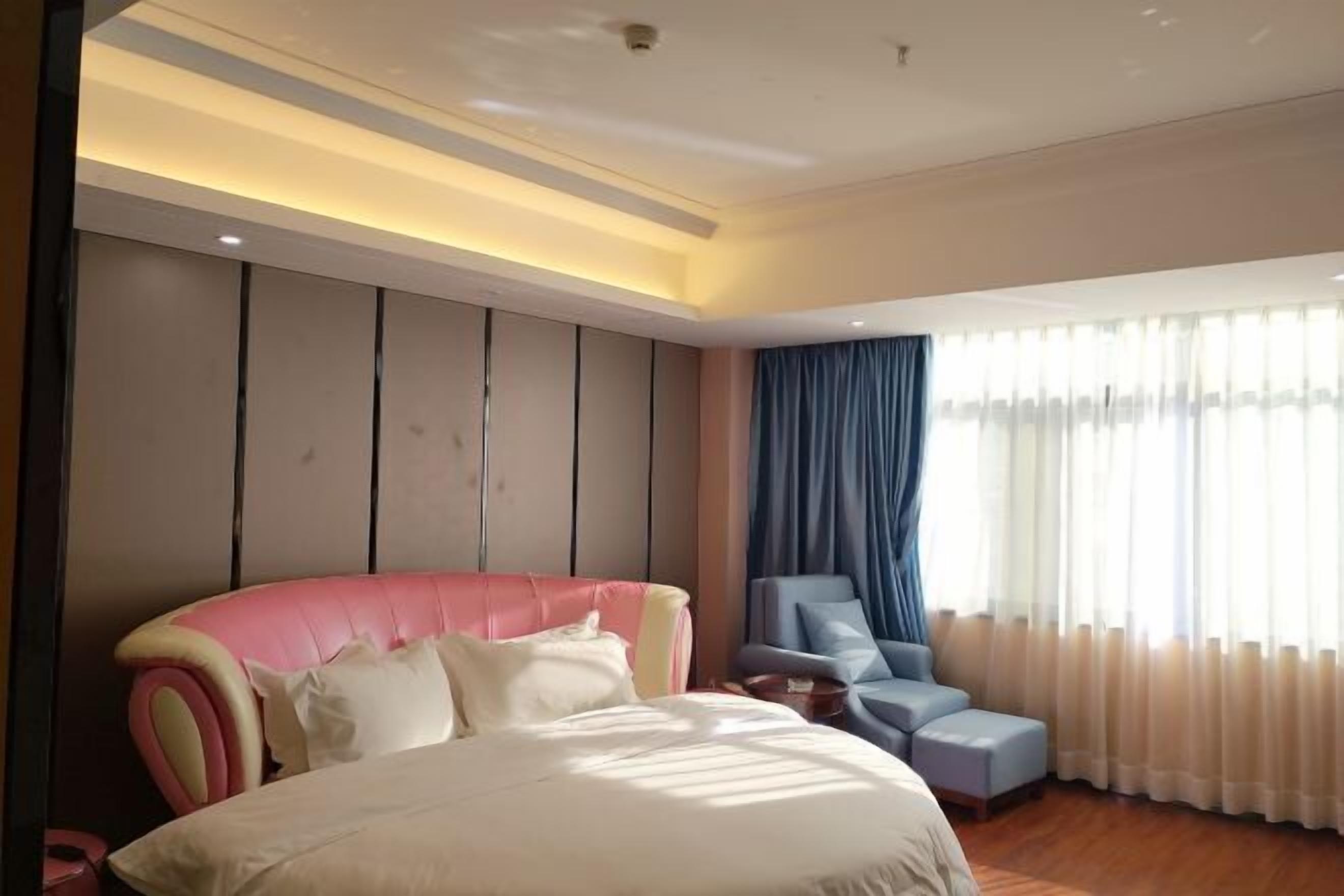 A modern bedroom with a large bed, a seating area with a chair, and a large window with curtains.
