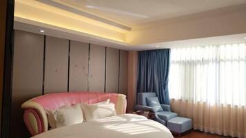 A modern bedroom with a large bed, a seating area with a chair, and a large window with curtains.