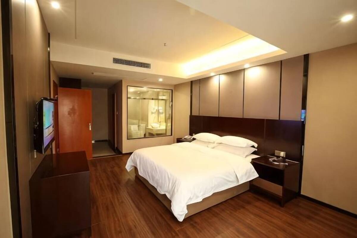 A hotel room with a bed, bedside table, TV, wardrobe, and a mirror.