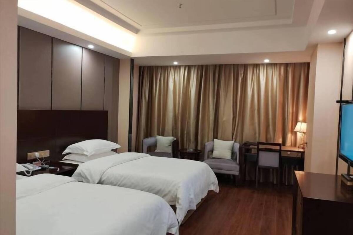 A hotel room with two beds, a desk, a chair, a TV, and a curtain.