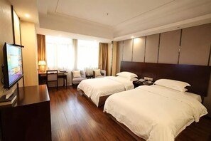 Ein Hotelzimmer mit zwei Betten, einem Schreibtisch, einem Fernseher und einem Fenster mit Vorhängen.