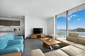 Enjoy a serene view of the sea from this stylish living room with a large window, flat-screen TV, and comfortable seating area.