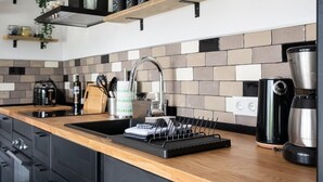 A modern kitchen with black cabinets, a wooden countertop, and a backsplash. There are shelves above the sink holding jars and a coffee maker. - Suite Swimming Pool Quinta da Eira 140 years old (Loule)