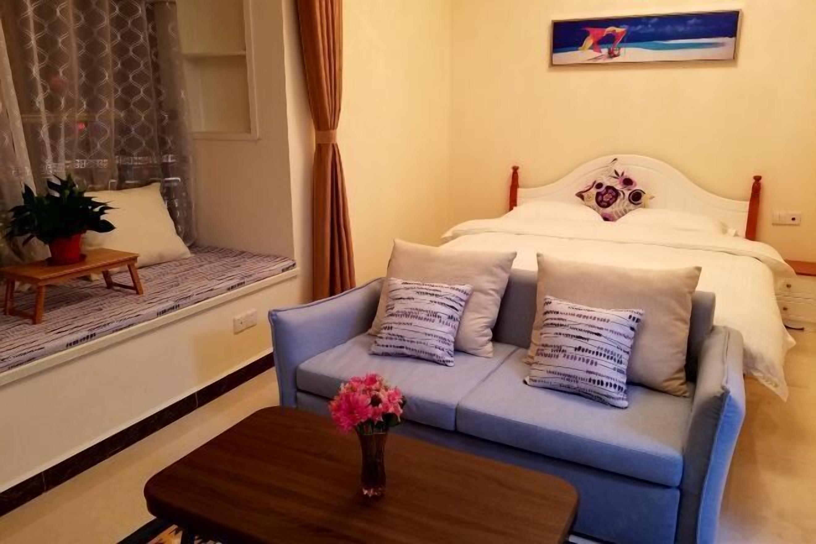A bedroom with a bed, a sofa, a small table with a vase of flowers, and a window with curtains.
