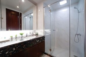 Un baño moderno con cabina de ducha de vidrio, lavabo de mármol y un espejo grande.