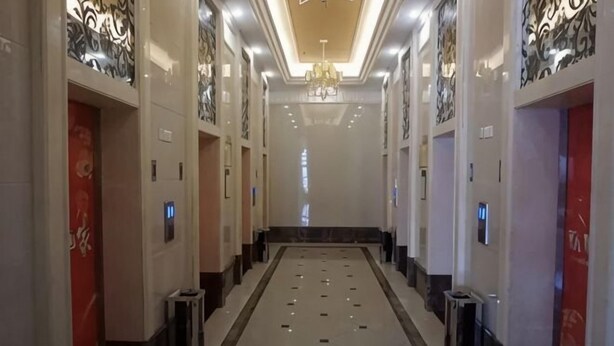 Un pasillo largo y estrecho con suelo reflectante, puertas a ambos lados y un candelabro.
