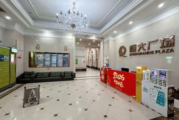 Un hall d’hôtel agrémenté d’un lustre, d’un comptoir d’accueil et d’une enseigne indiquant « EverGrande Plaza ».